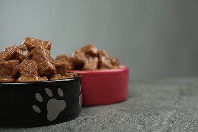 Wet pet food in feeding bowls on grey table, closeup. Space for text