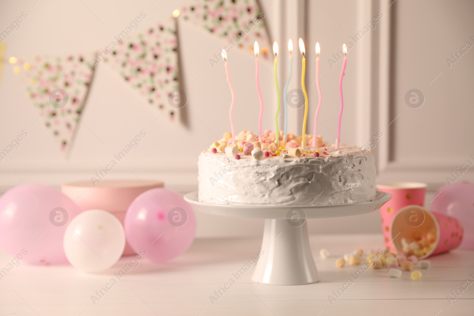 Photo of Tasty Birthday cake with burning candles and party decor on white table