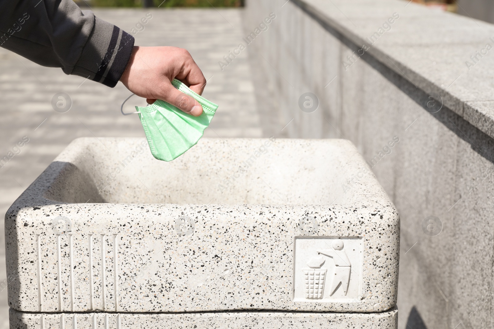 Photo of Man throwing medical mask into trash bin outdoors, closeup