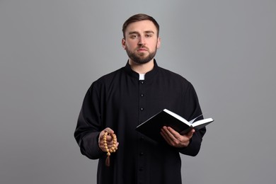 Photo of Priest with beads and Bible praying on grey background