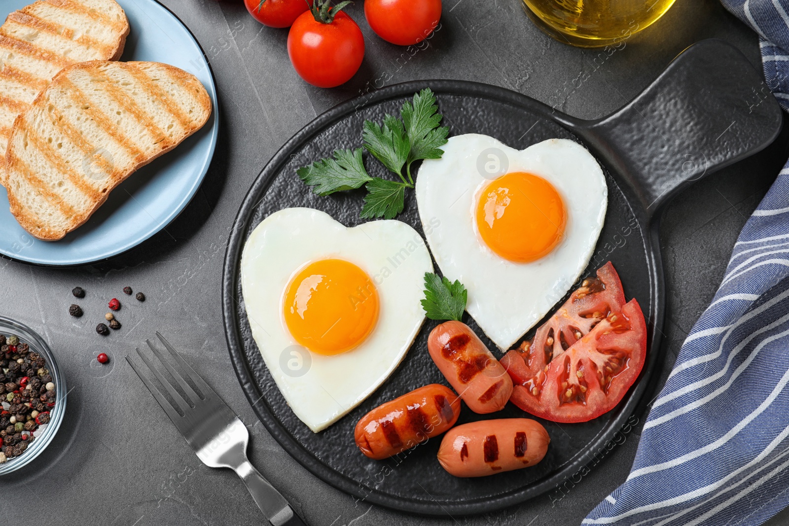 Photo of Delicious breakfast with heart shaped fried eggs and  sausages served on dark grey table, flat lay