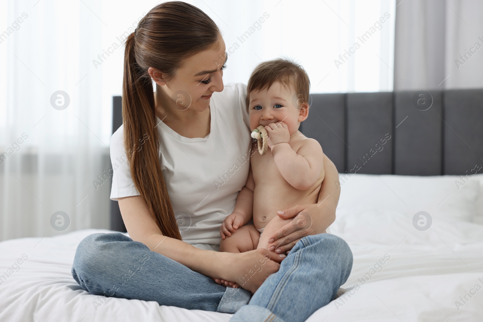 Photo of Happy mother sitting with her baby on bed at home