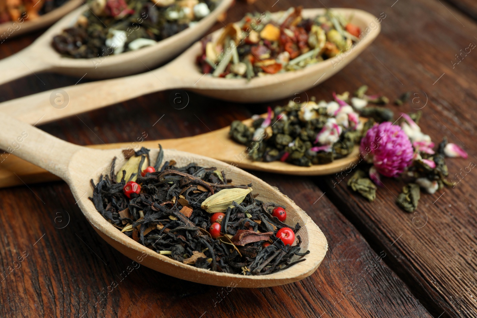 Photo of Spoons with dried herbal tea leaves on wooden table, closeup