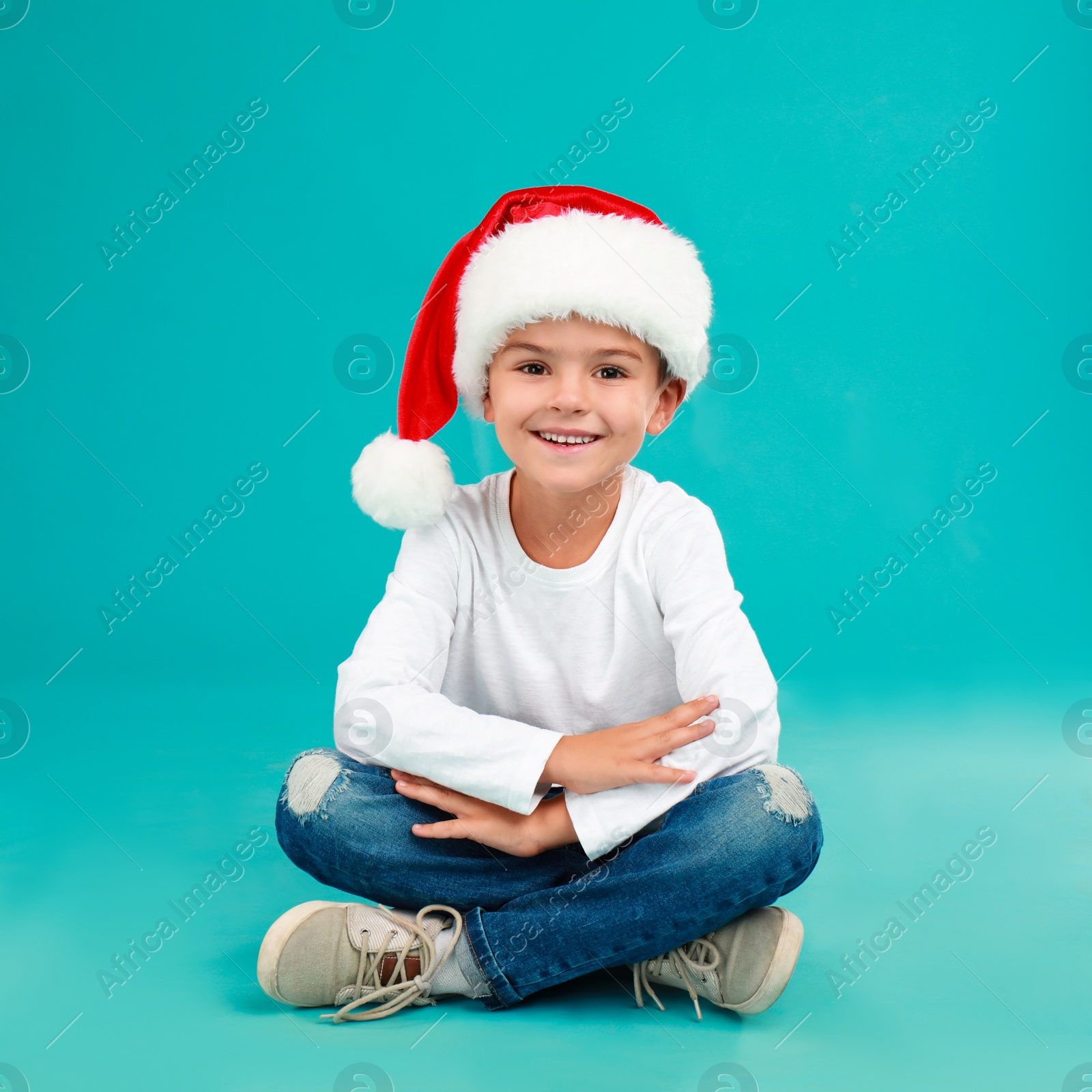 Photo of Cute little child wearing Santa hat on light blue background. Christmas holiday