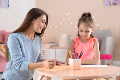 Photo of Cute little child drawing at table with her mother in playing room