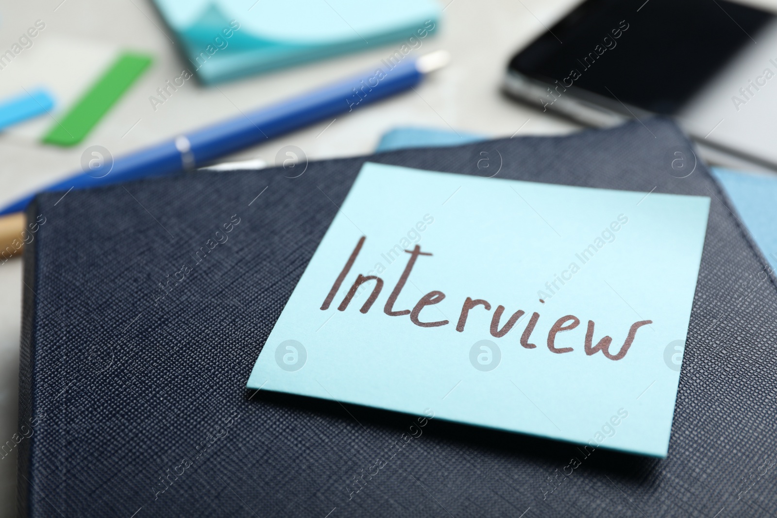 Photo of Reminder note about job interview and stationery on table, closeup