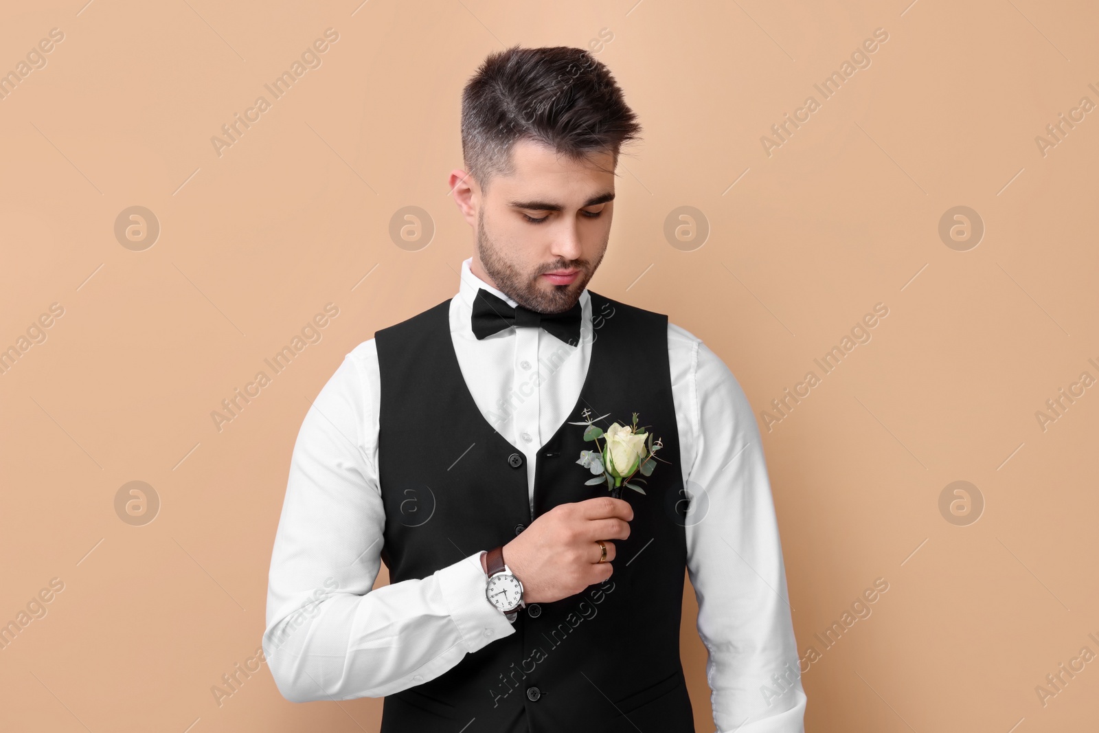 Photo of Handsome young groom with boutonniere on beige background. Wedding accessory