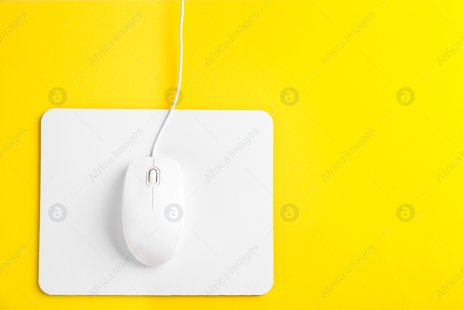 Photo of Modern wired optical mouse and pad on yellow background, top view. Space for text