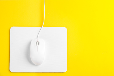 Photo of Modern wired optical mouse and pad on yellow background, top view. Space for text