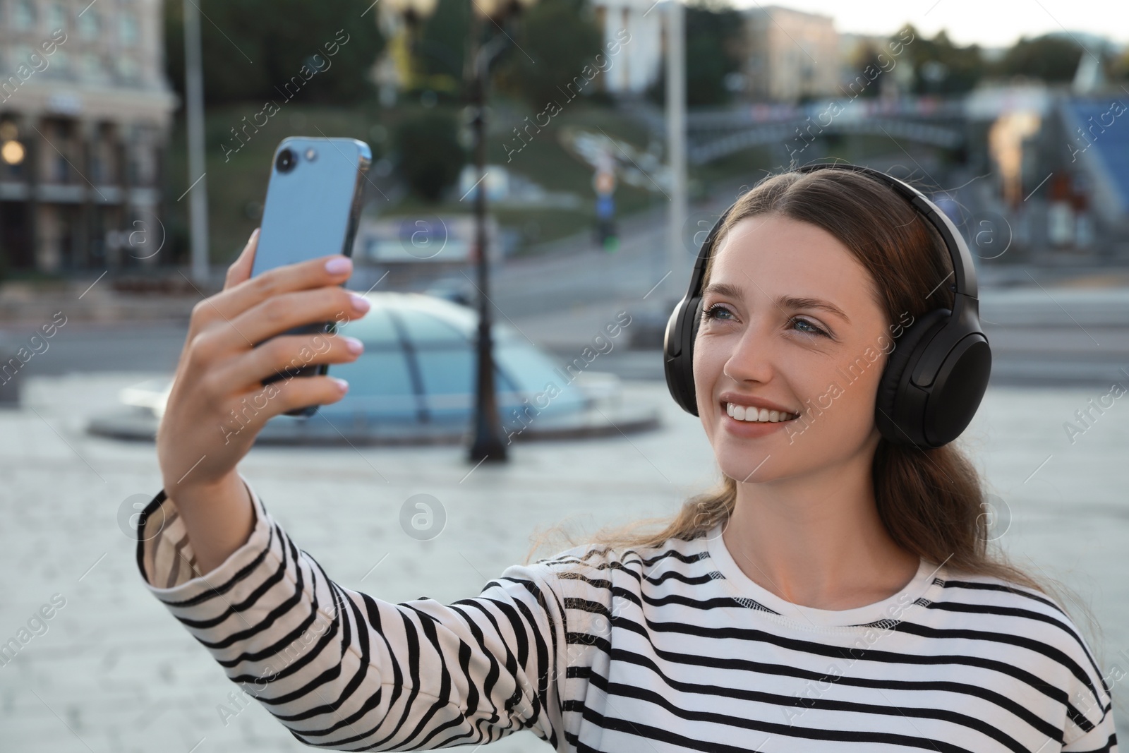 Photo of Smiling woman in headphones taking selfie on city street