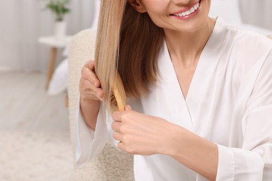 Photo of Woman brushing her hair indoors, closeup view