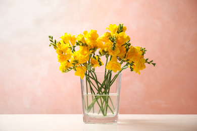 Beautiful blooming yellow freesias in glass vase on table against pink background