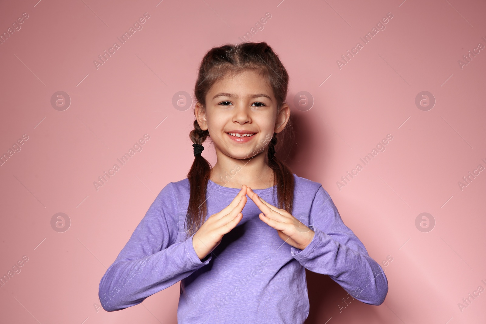 Photo of Little girl showing HOUSE gesture in sign language on color background