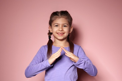 Photo of Little girl showing HOUSE gesture in sign language on color background