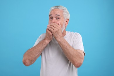 Photo of Portrait of embarrassed senior man covering mouth on light blue background