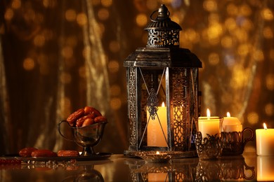 Photo of Arabic lantern, burning candles, dates and misbaha on mirror surface against blurred lights