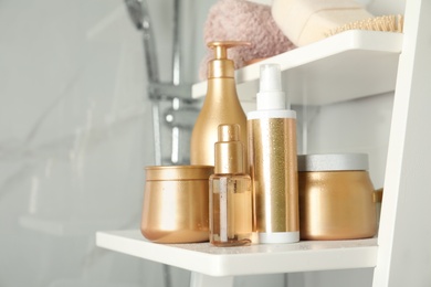 Set of hair care cosmetic products covered with water drops on white rack in bathroom