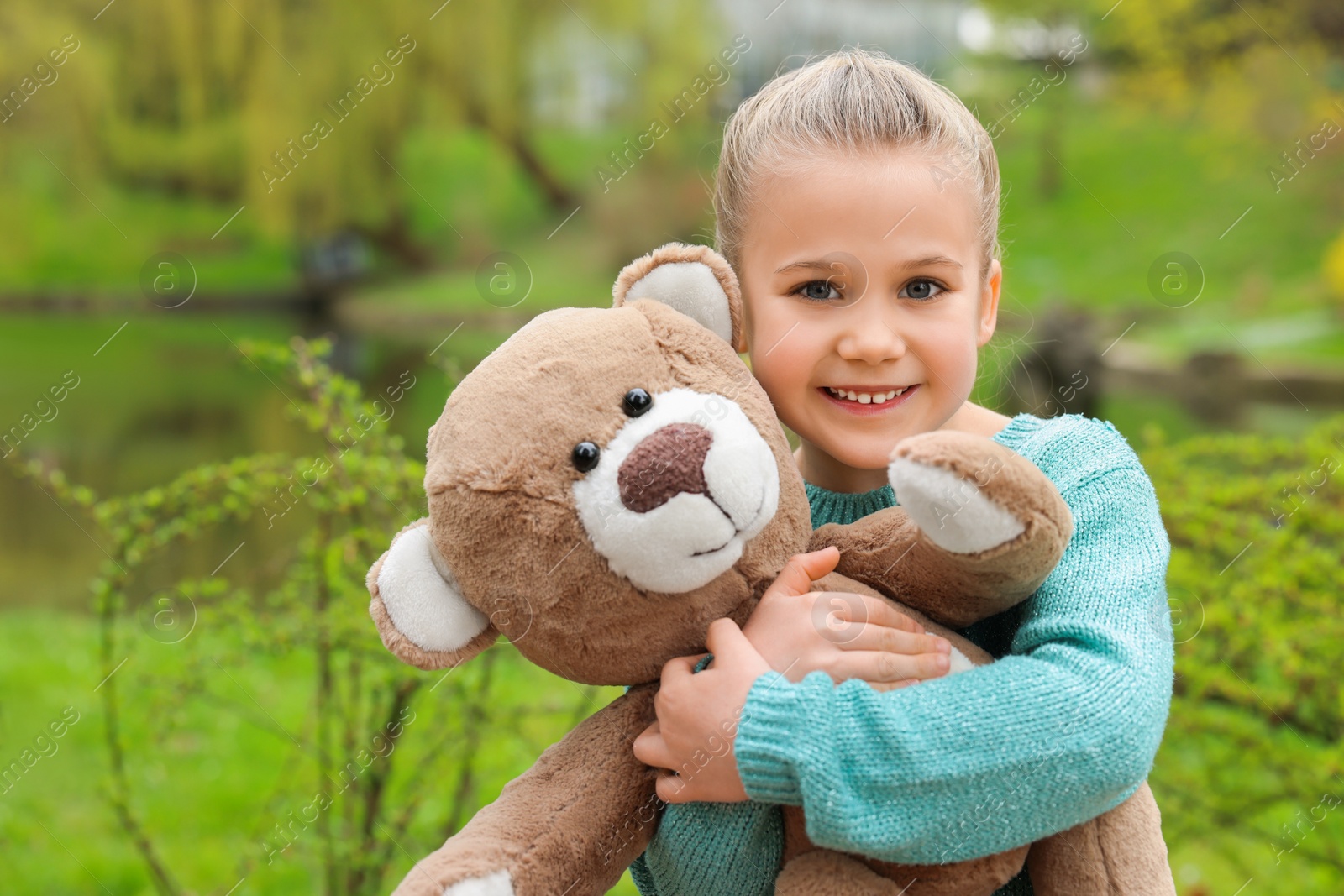 Photo of Cute little girl with teddy bear outdoors