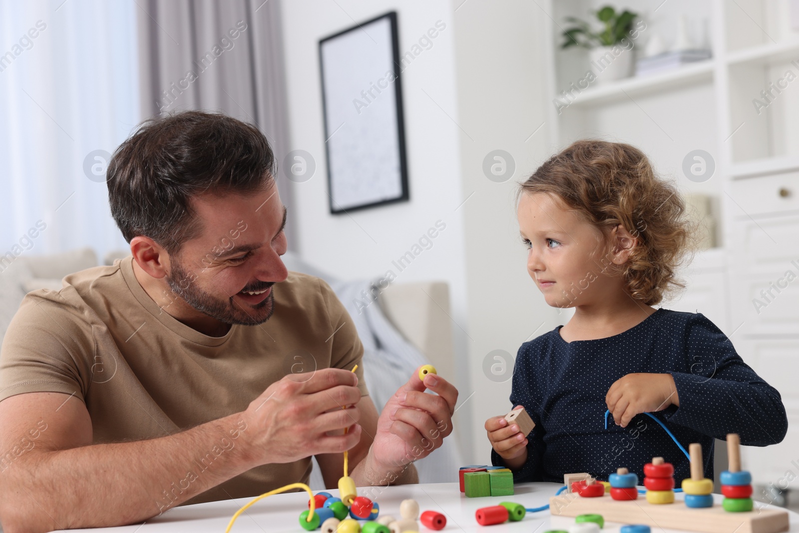 Photo of Motor skills development. Father and daughter playing with wooden pieces and strings for threading activity at table indoors