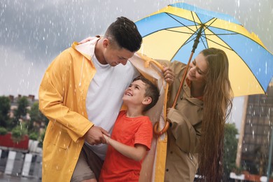 Photo of Happy family with umbrella walking under rain on city street