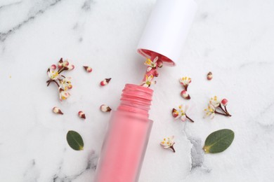 Photo of Pink lip gloss, flowers and green leaves on white marble table, flat lay