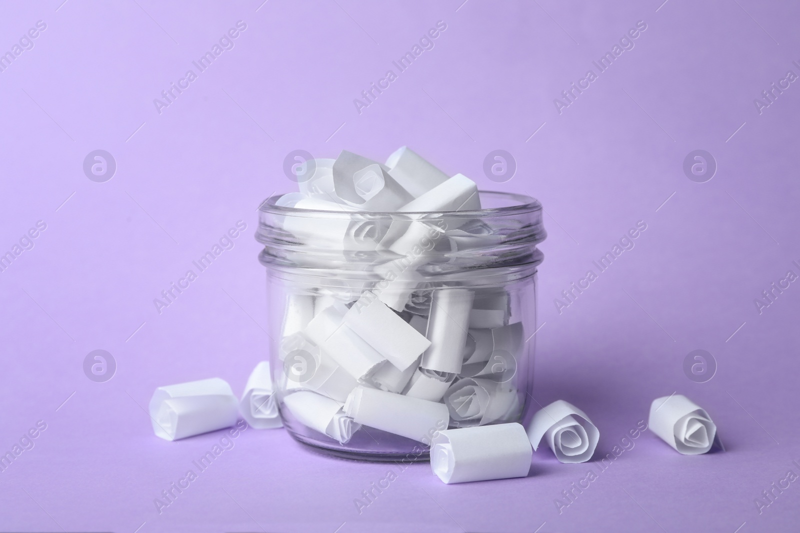 Photo of Glass jar full of rolled paper sheets on violet background