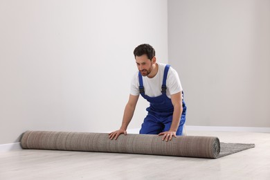 Photo of Worker unrolling new carpet on floor in room