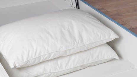 Storage drawer under bed with white pillows indoors, closeup