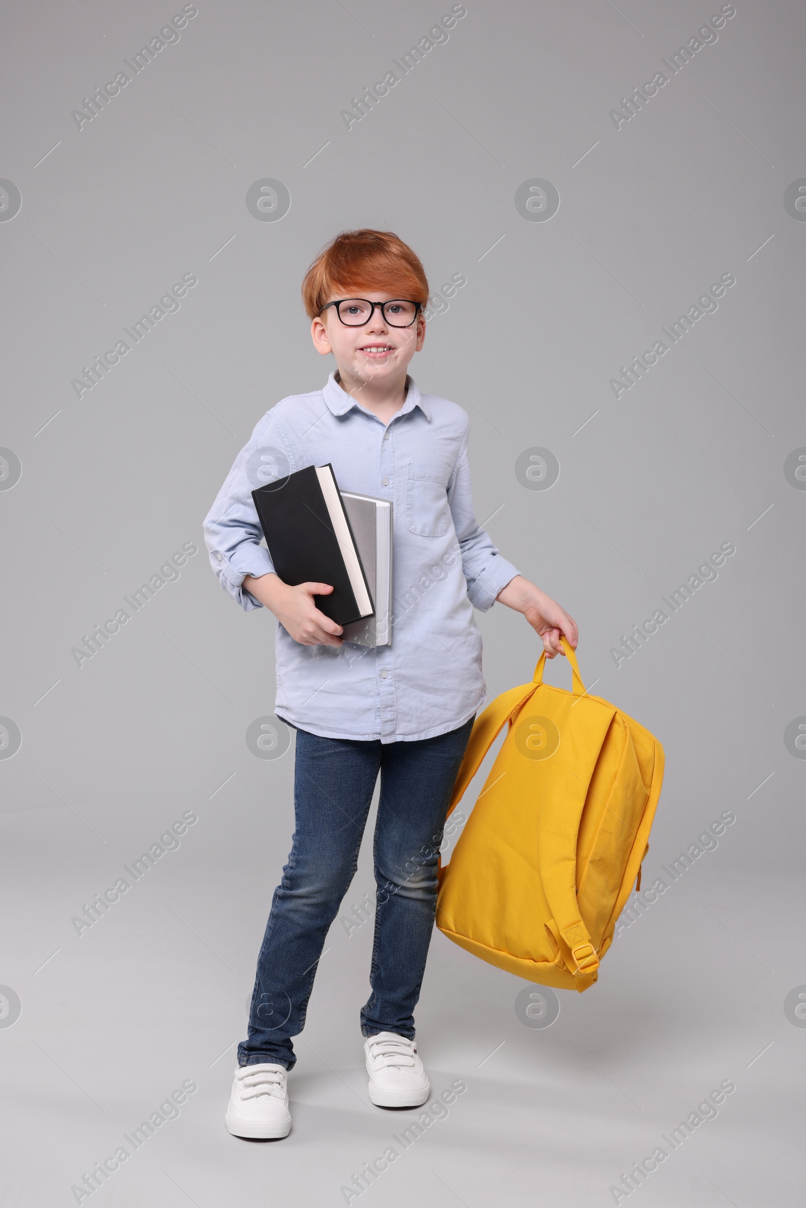 Photo of Happy schoolboy with books and backpack on grey background