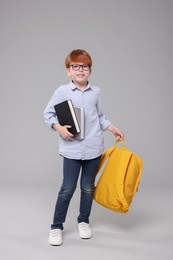 Happy schoolboy with books and backpack on grey background