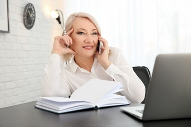 Photo of Mature woman talking on mobile phone at workplace