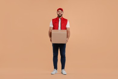 Photo of Happy young courier with parcel on light brown background