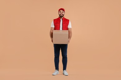 Happy young courier with parcel on light brown background