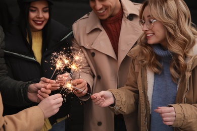 Photo of People in warm clothes holding burning sparklers on dark background