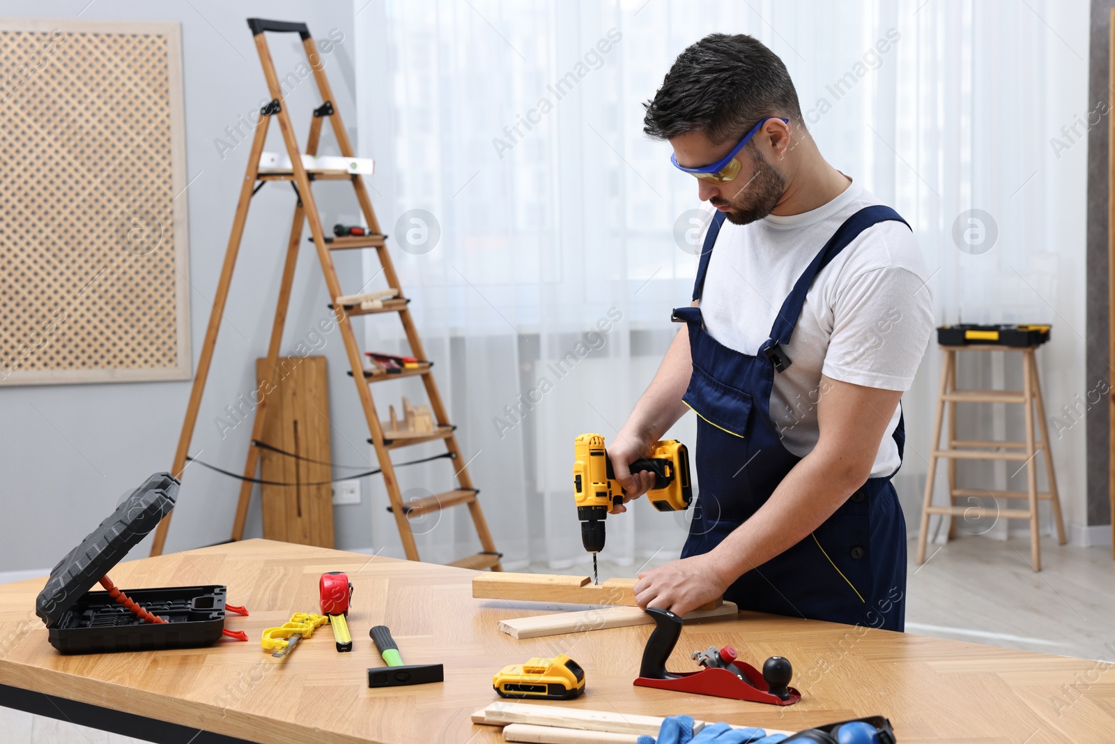 Photo of Young worker using electric drill at table in workshop