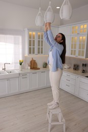 Woman on ladder changing lightbulb in ceiling lamp at home