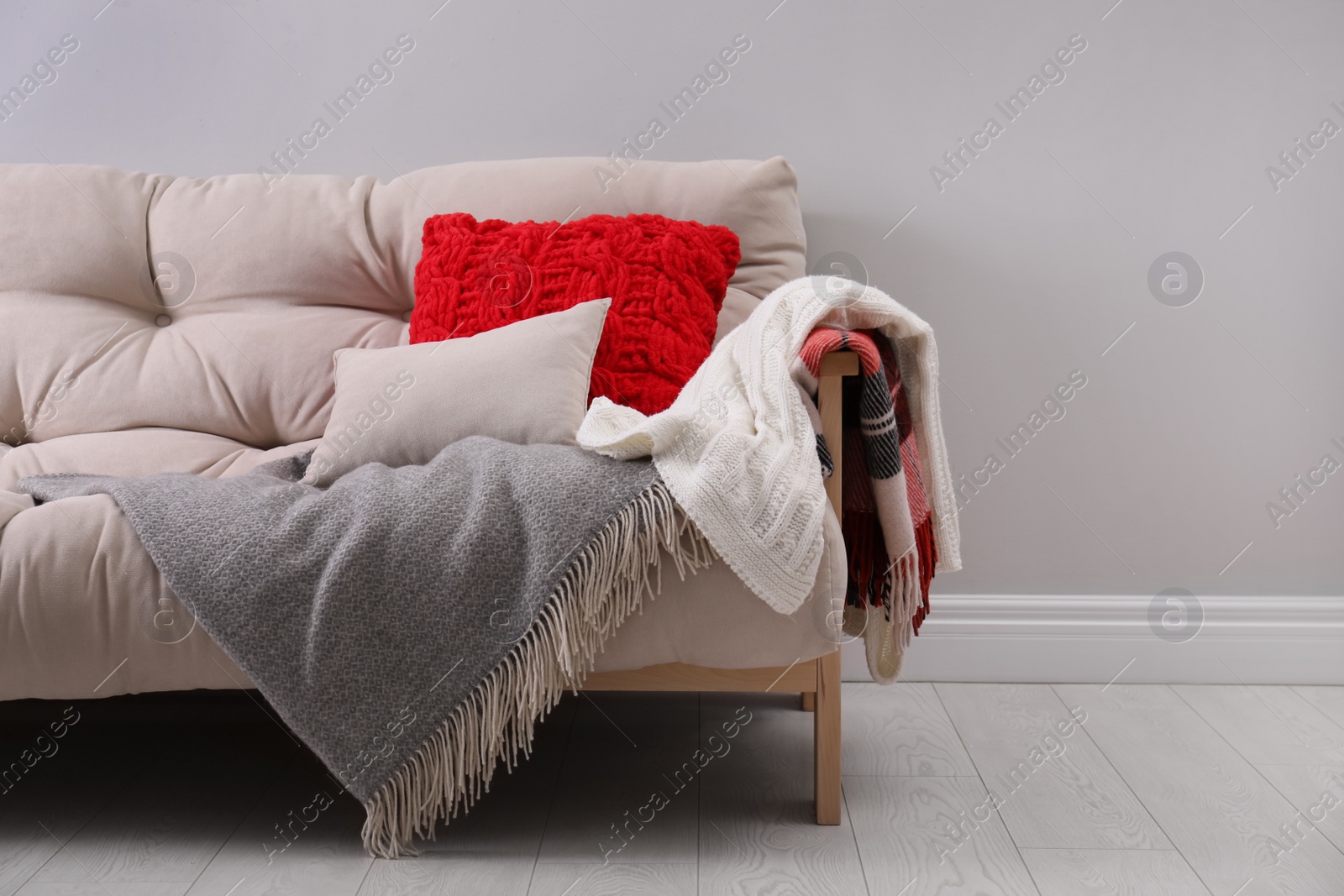 Photo of Sofa with soft pillows and warm plaids near light wall indoors