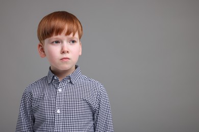 Portrait of sad little boy on grey background, space for text