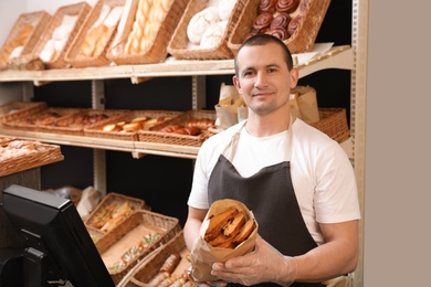 Photo of Professional baker holding paper bag with pastry in store
