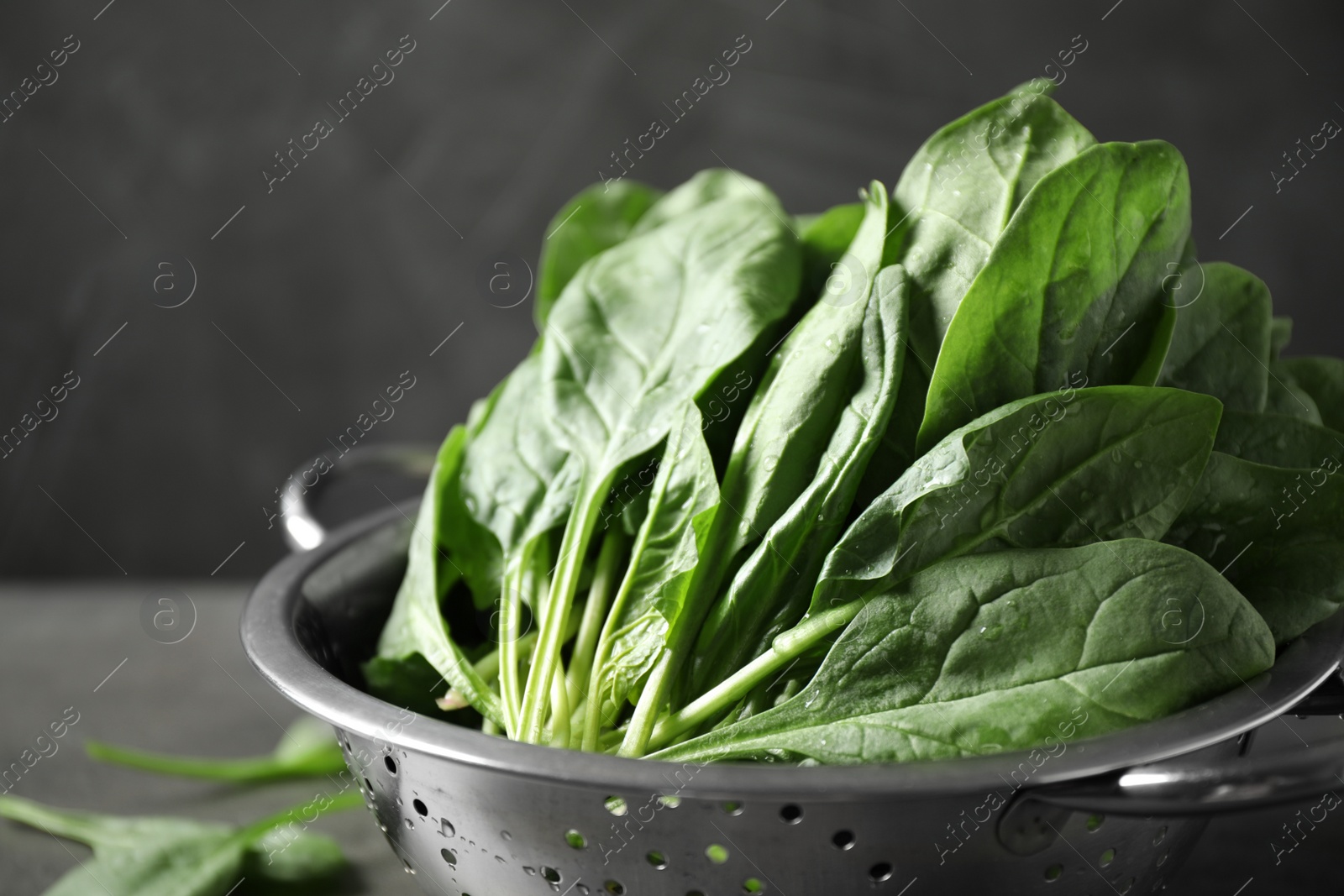 Photo of Colander with fresh green healthy spinach on table, closeup