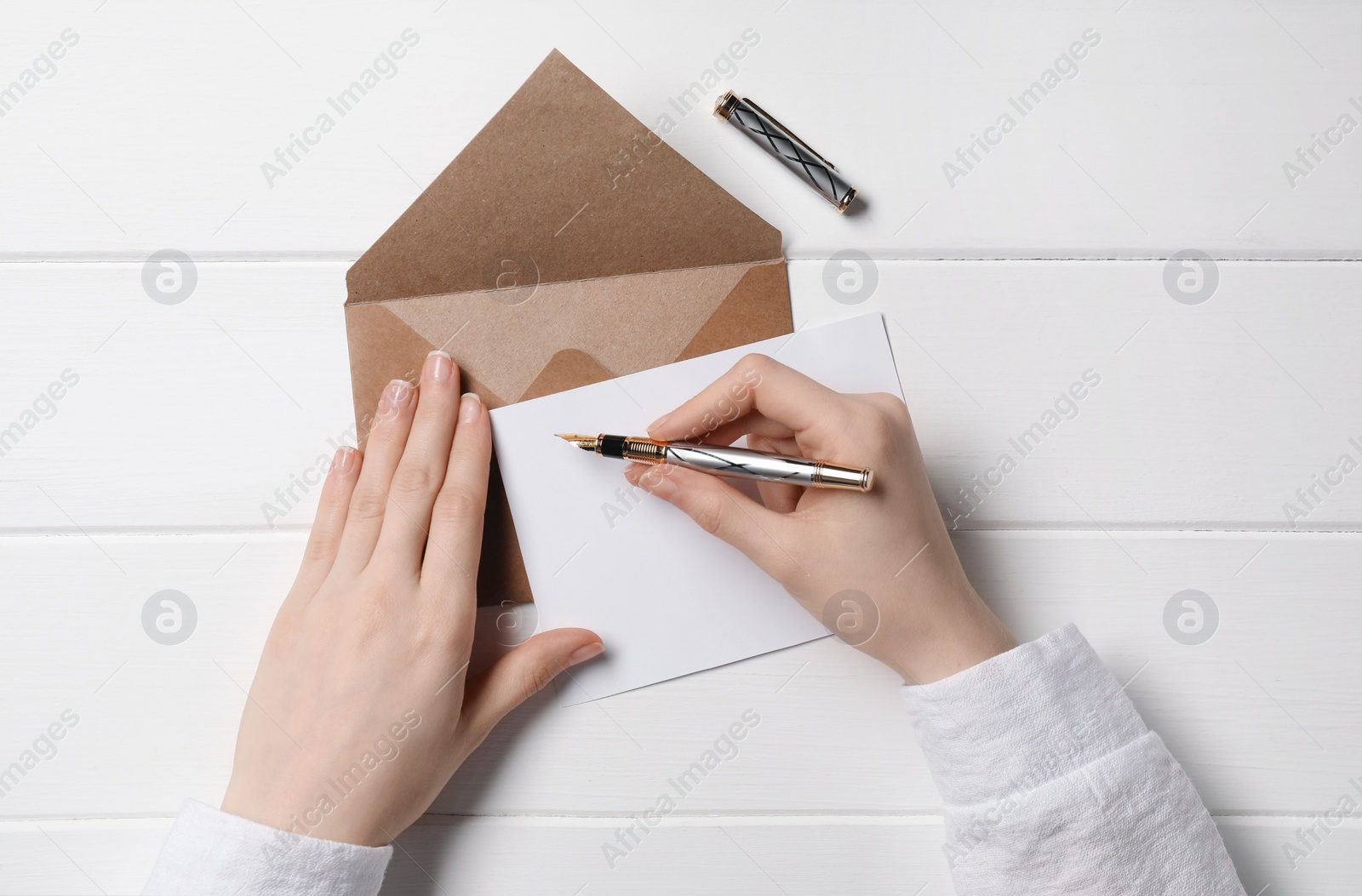 Photo of Woman writing letter at white wooden table, top view
