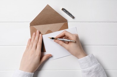 Woman writing letter at white wooden table, top view