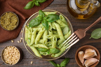 Delicious pasta with pesto sauce and ingredients on wooden table, flat lay