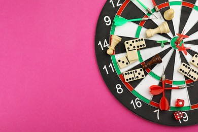 Photo of Dart board with components of tabletop games on pink background, top view. Space for text
