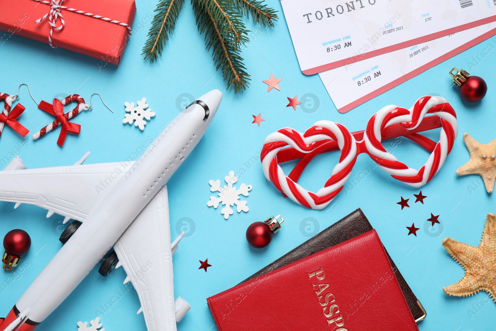 Photo of Flat lay composition with Christmas decorations, toy airplane and passports on light blue background. Winter vacation