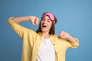 Photo of Young tired woman with sleeping mask yawning on light blue background