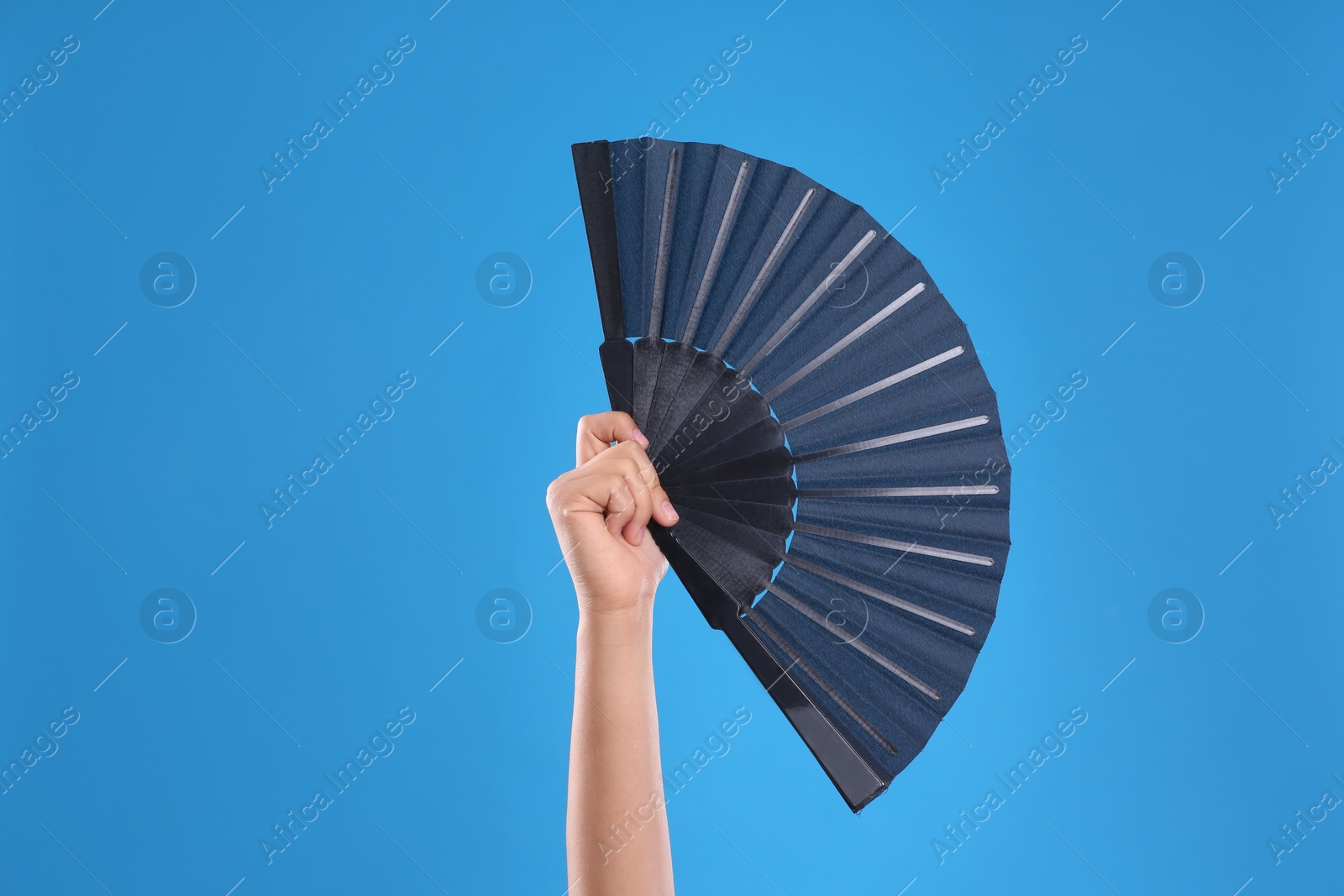 Photo of Woman holding black hand fan on light blue  background, closeup