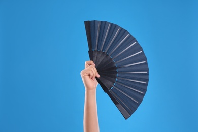 Woman holding black hand fan on light blue  background, closeup