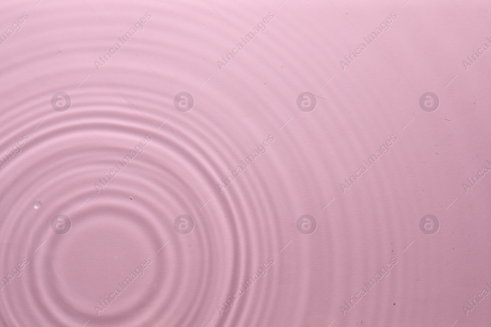 Photo of Rippled surface of clear water on pink background, top view