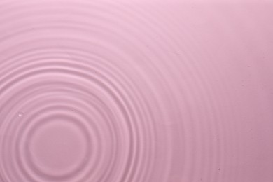 Rippled surface of clear water on pink background, top view